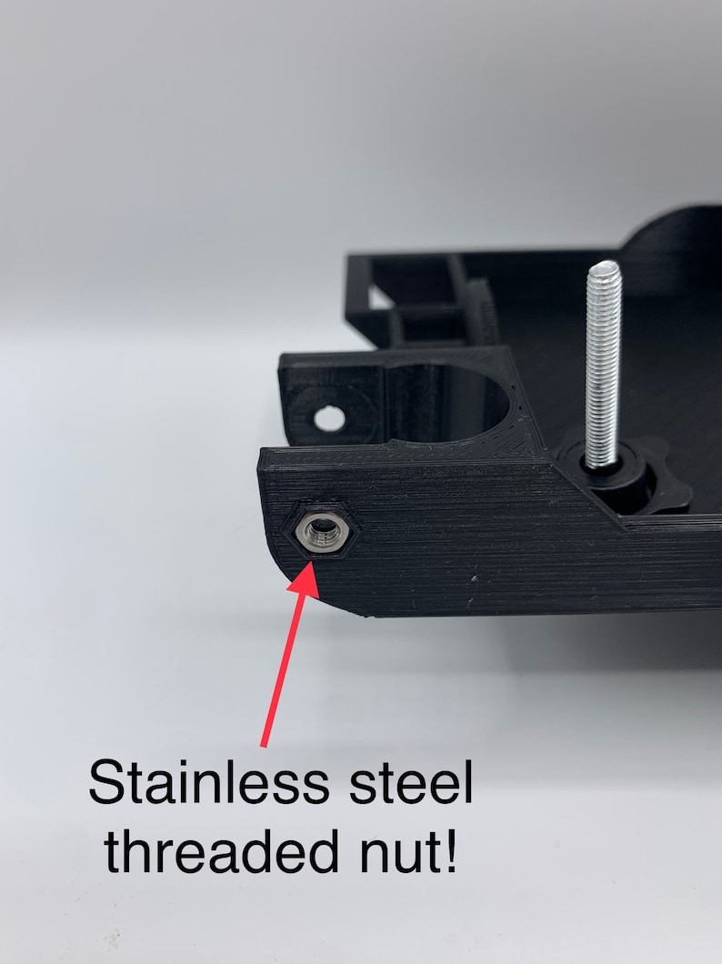 May include: Close-up of a black 3D printed object with a stainless steel threaded nut. The nut is visible in the lower left corner of the image.