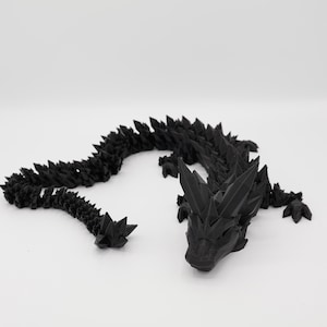 May include: A black 3D printed dragon figurine with a spiky, crystalline design. The dragon is curled up with its tail tucked under its body.
