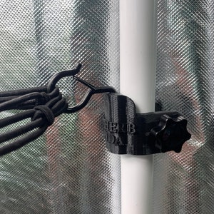 Pode incluir: Gancho de rede de plástico preto com uma manivela para apertar. O gancho está preso a um poste branco e tem as palavras "Herb Panda" impressas.