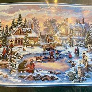 May include: Cross-stitch artwork showing a winter scene with snow-covered houses, a frozen pond, and figures ice skating. The artwork features a bridge, trees, and lampposts, with a warm, inviting colour palette. The scene evokes a sense of holiday cheer.