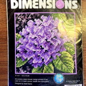 May include: A Dimensions needlepoint kit titled Lovely Hydrangea, model 7189. The packaging features a purple hydrangea flower design, measuring 5 inches by 5 inches. It includes cotton thread, a 12 mesh canvas, a needle, and instructions.