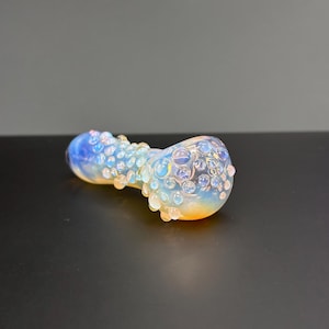 May include: A glass pipe with a blue and white iridescent finish. The pipe is covered in small, raised bubbles.