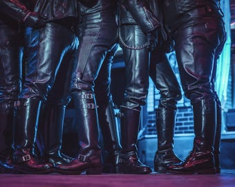 May include: Five people wearing black leather pants and boots. The boots are tall and have buckles. The people are standing in a row, and their legs are close together.