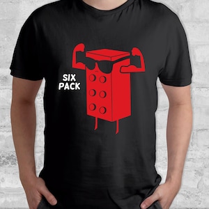 Puede incluir: Camiseta negra con un gráfico rojo de un six-pack con gafas de sol y flexionando los brazos. Las palabras "SIX PACK" están impresas en blanco. La camiseta está hecha de un material suave.