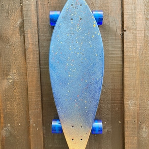 May include: A blue and gold longboard skateboard with blue wheels. The deck is painted with a blue and gold gradient and has a speckled pattern.