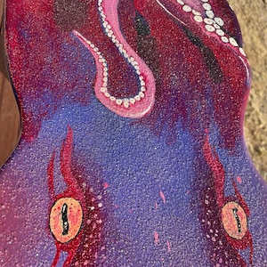 May include: A purple and red ukulele with a glitter finish and a painted image of an octopus with pink tentacles.