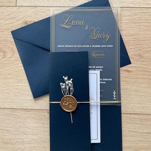 Peut inclure: Une invitation de mariage bleu marine avec un recouvrement transparent sur lequel sont inscrits les noms "Lena & Gary" en écriture dorée. L'invitation comprend le texte "Seront heureux de vous inviter à célébrer leur union" et "Septembre" en écriture dorée. L'invitation est liée avec de la ficelle et un sceau de cire.