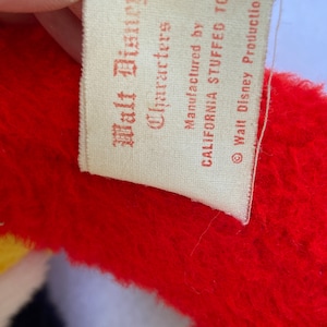 May include: A white tag with red text that reads "Walt Disney Characters" and "Manufactured by California Stuffed Toys" with a copyright symbol and "Walt Disney Productions".