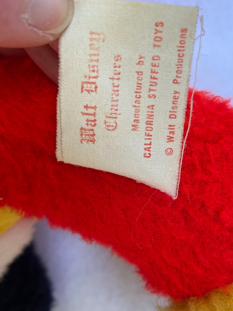 May include: A white tag with red text that reads "Walt Disney Characters" and "Manufactured by California Stuffed Toys" with a copyright symbol and "Walt Disney Productions".