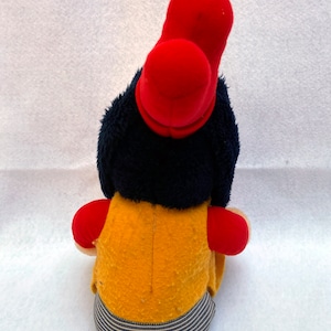 May include: A plush toy with a red hat, blue hair, a yellow vest, and blue and white striped pants.
