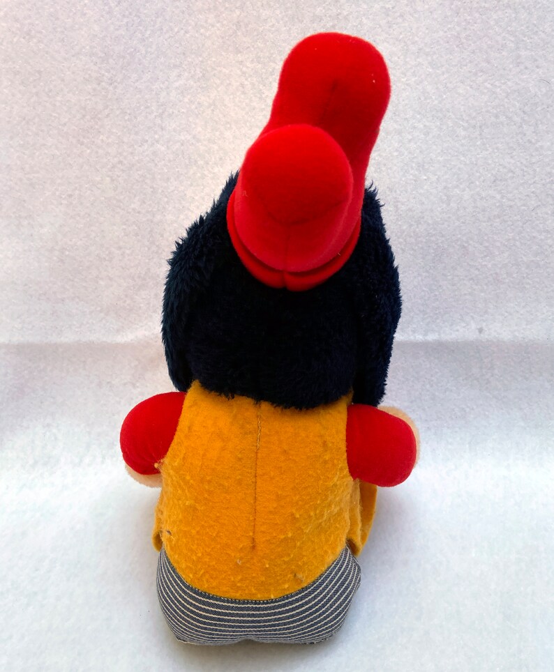May include: A plush toy with a red hat, blue hair, a yellow vest, and blue and white striped pants.