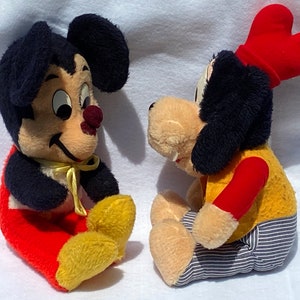 May include: Two vintage plush toys, a black and white mouse wearing red pants and a yellow bow, and a black and white dog wearing a red hat, yellow shirt, and blue and white striped pants.