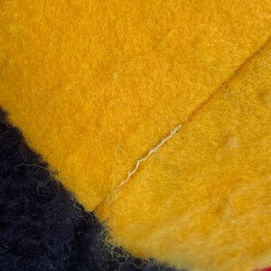 May include: Close-up of a yellow, black, and red plush toy. The toy is made of soft, fuzzy fabric and has a seam running down the center of the yellow section.