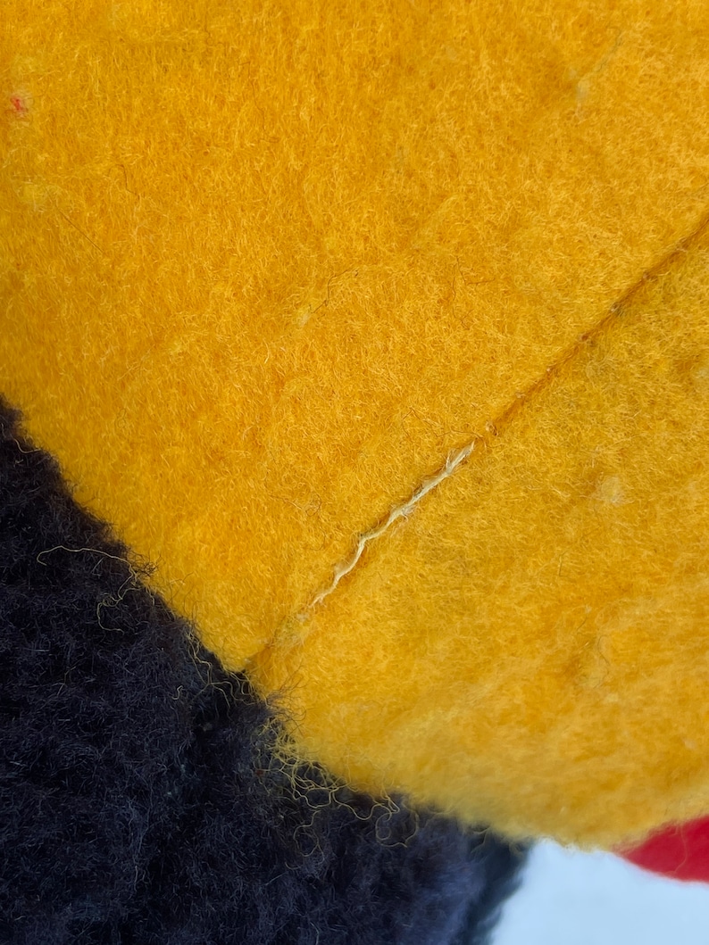 May include: Close-up of a yellow, black, and red plush toy. The toy is made of soft, fuzzy fabric and has a seam running down the center of the yellow section.