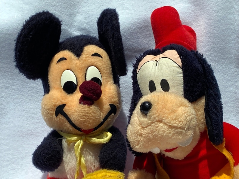May include: A plush Mickey Mouse and Goofy toy set. Mickey Mouse is wearing a yellow bow tie and Goofy is wearing a red hat.