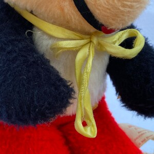 May include: A plush toy with black fur arms, red pants, and a yellow ribbon around its neck. The toy has a white face with a black nose and a red heart on its chest.
