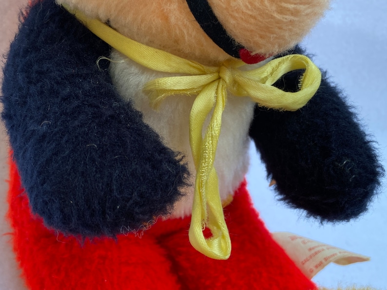 May include: A plush toy with black fur arms, red pants, and a yellow ribbon around its neck. The toy has a white face with a black nose and a red heart on its chest.