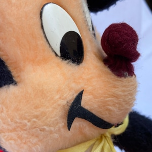May include: Close-up of a plush toy with black fur, a peach-colored face, a black mustache, a large white eye with a black pupil, and a maroon nose.