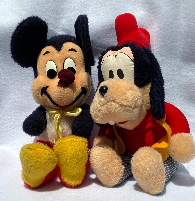 May include: A vintage plush Mickey Mouse and Goofy toy set. Mickey Mouse is wearing a yellow bow tie and red shoes. Goofy is wearing a red hat and a red and yellow shirt.