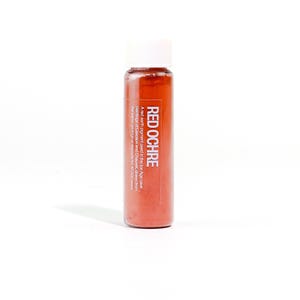 May include: A small glass bottle filled with red ochre pigment. The label reads "RED OCHRE" and describes its use in Ice Age cave paintings. The bottle has a white cap and is set against a white background.