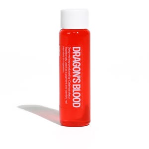 May include: A small, cylindrical bottle filled with a deep red liquid, labeled "DRAGON'S BLOOD" in white text. The bottle has a white cap and a description on the side. The liquid is traditionally used as a pigment and varnish.