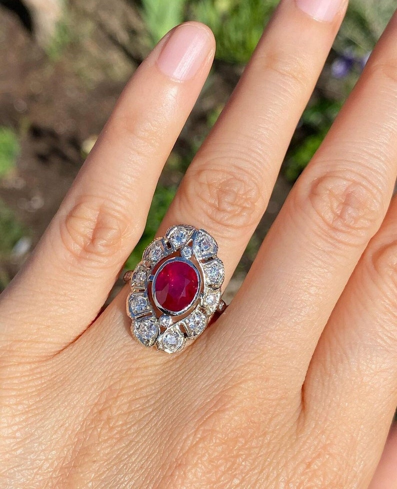 May include: A silver ring with a large oval ruby surrounded by smaller diamonds.