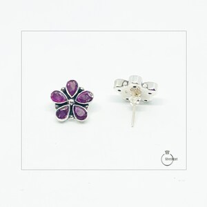 May include: A pair of silver flower-shaped earrings with purple gemstones. The earrings have a post back.