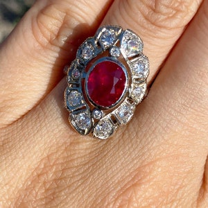 May include: A ring with a large oval ruby surrounded by a halo of smaller diamonds. The ring is set in white gold.