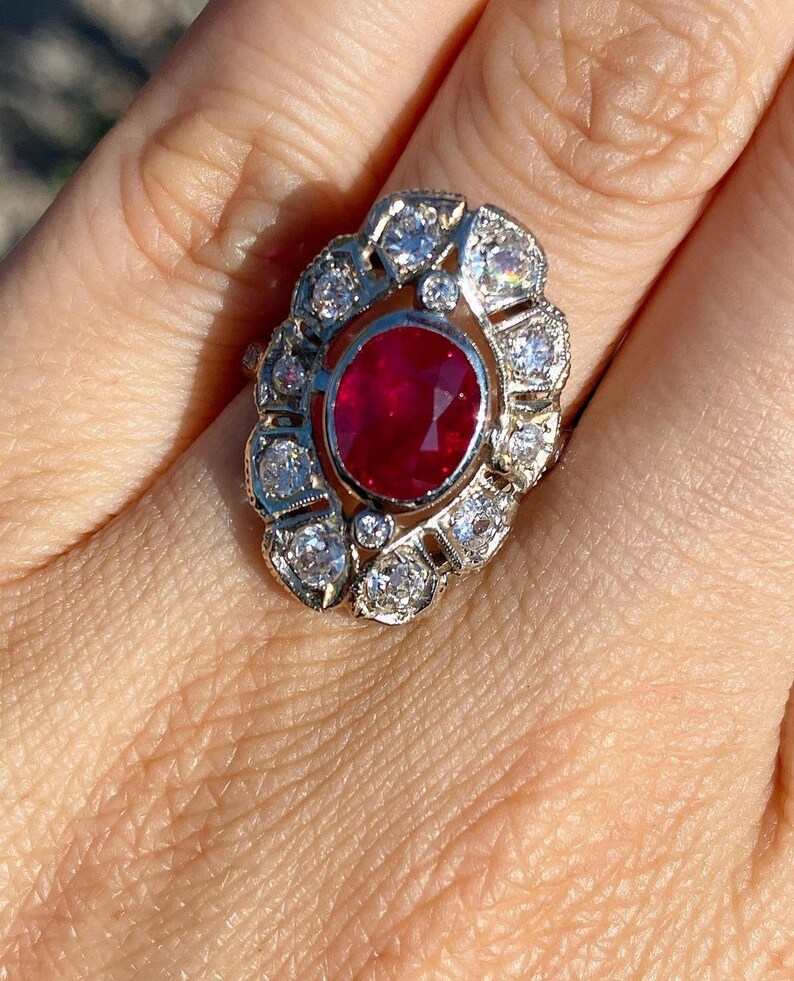 May include: A ring with a large oval ruby surrounded by a halo of smaller diamonds. The ring is set in white gold.
