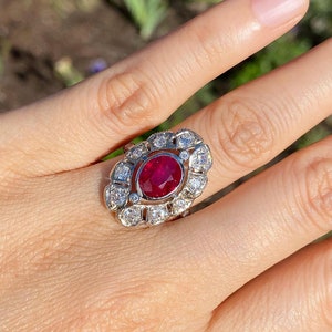 May include: A ring with a large oval ruby surrounded by smaller diamonds. The ring is set in white gold and has a delicate floral design.