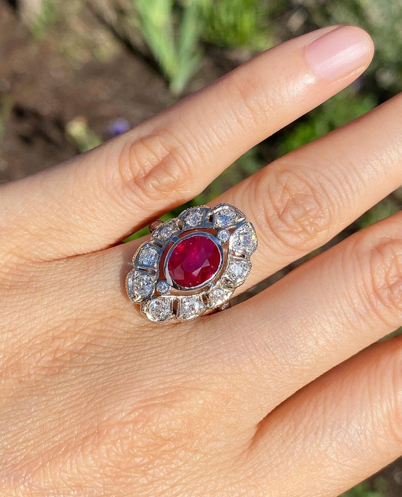 May include: A ring with a large oval ruby surrounded by smaller diamonds. The ring is set in white gold and has a delicate floral design.