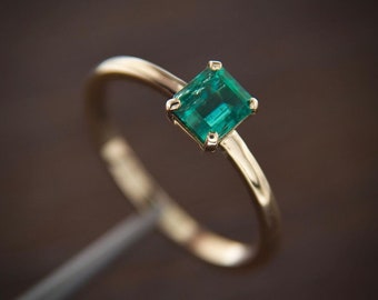 Op de afbeelding: Een gouden ring met een vierkante smaragdgroene edelsteen.