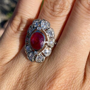 May include: A silver ring with a large red ruby surrounded by smaller diamonds. The ring is set in a floral design.