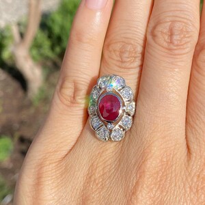 May include: A ring with a large oval ruby surrounded by smaller diamonds. The ring is set in white gold.