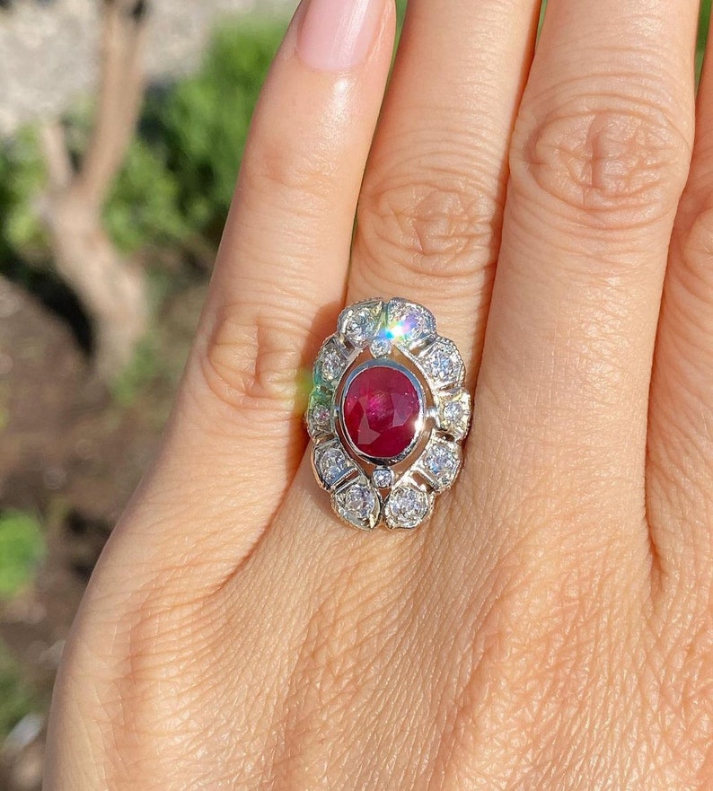 May include: A ring with a large oval ruby surrounded by smaller diamonds. The ring is set in white gold.