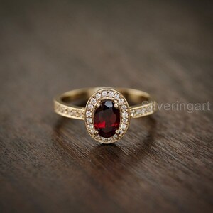 May include: A gold ring with a large oval-shaped red gemstone surrounded by a halo of smaller clear gemstones.
