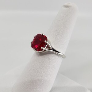 May include: A silver ring featuring a large, red, cushion-cut gemstone.