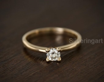 May include: A gold band engagement ring with a single round diamond.