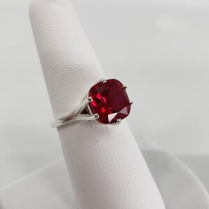May include: A silver ring featuring a large, red, cushion-cut gemstone.