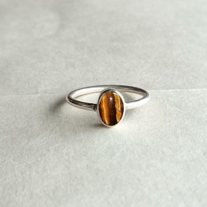 May include: A silver ring with an oval-shaped tiger's eye gemstone.