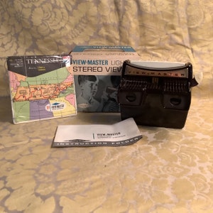 Könnte beinhalten: Ein Vintage View-Master-Set mit einem schwarzen Betrachter, einer Box mit der Aufschrift "VIEW-MASTER LIGHT STEREO VIEW" und einem Heft mit dem Titel "TENNESSEE" mit einer Karte.