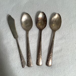 Puede incluir: Un conjunto de cubiertos antiguos, que incluye tres cucharas y un cuchillo de mantequilla. Las cucharas y el cuchillo son de color plateado con detalles florales ornamentados en los mangos. Las cucharas tienen cuencos ovalados y el cuchillo tiene una hoja redondeada.