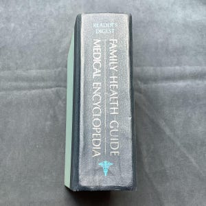 Może przedstawiać: Książka Reader's Digest Family Health Guide Medical Encyclopedia. Grzbiet jest ciemnoszary z białymi i turkusowymi literami. Krawędź książki jest jasnozielona.