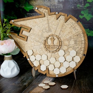 May include: Wooden Star Wars Millennium Falcon guest book with a hexagonal honeycomb design. The guest book is personalized with the names "Daniel & Amanda" and the date "April 23rd 2020".