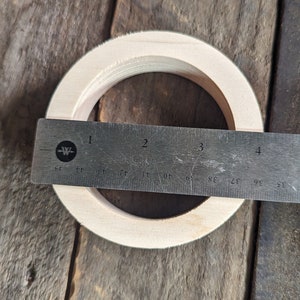 May include: A wooden ring with a diameter of 3 inches, measured with a ruler. The ring is light brown and has a smooth surface.