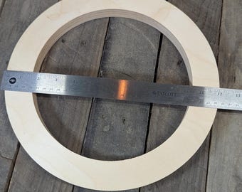 May include: Several unfinished wooden craft rings are displayed on a wooden surface. A metal ruler is placed across one ring, measuring its diameter. The rings appear to be approximately 12 inches in diameter, suitable for various DIY projects.