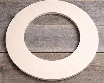 May include: A light-colored, unfinished wooden wreath form. The circular shape is made of a thick, solid piece of wood, perfect for crafting and DIY projects. The wreath is set against a rustic wooden background.
