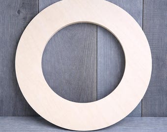 May include: A round, unfinished wooden wreath form. The wreath is made of light-colored wood and has a circular shape with a large, open center. The wood grain is visible, and the form is ready for customization.