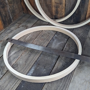 May include: A wooden hoop with a metal ruler measuring 16 inches across. The hoop is on a wooden surface.