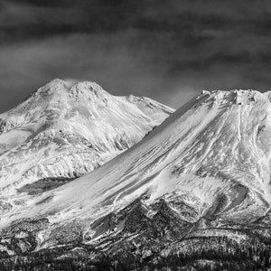 Puede incluir: Una fotografía en blanco y negro de dos montañas cubiertas de nieve contra un cielo nublado. Las montañas están cubiertas de nieve y tienen una superficie rugosa y texturizada.